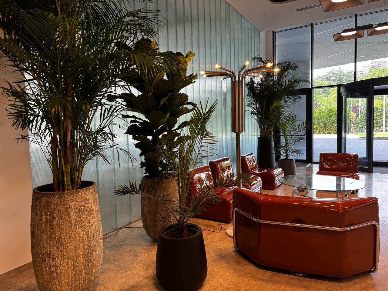 Red sofas around a glass table, with tall plants in the foreground