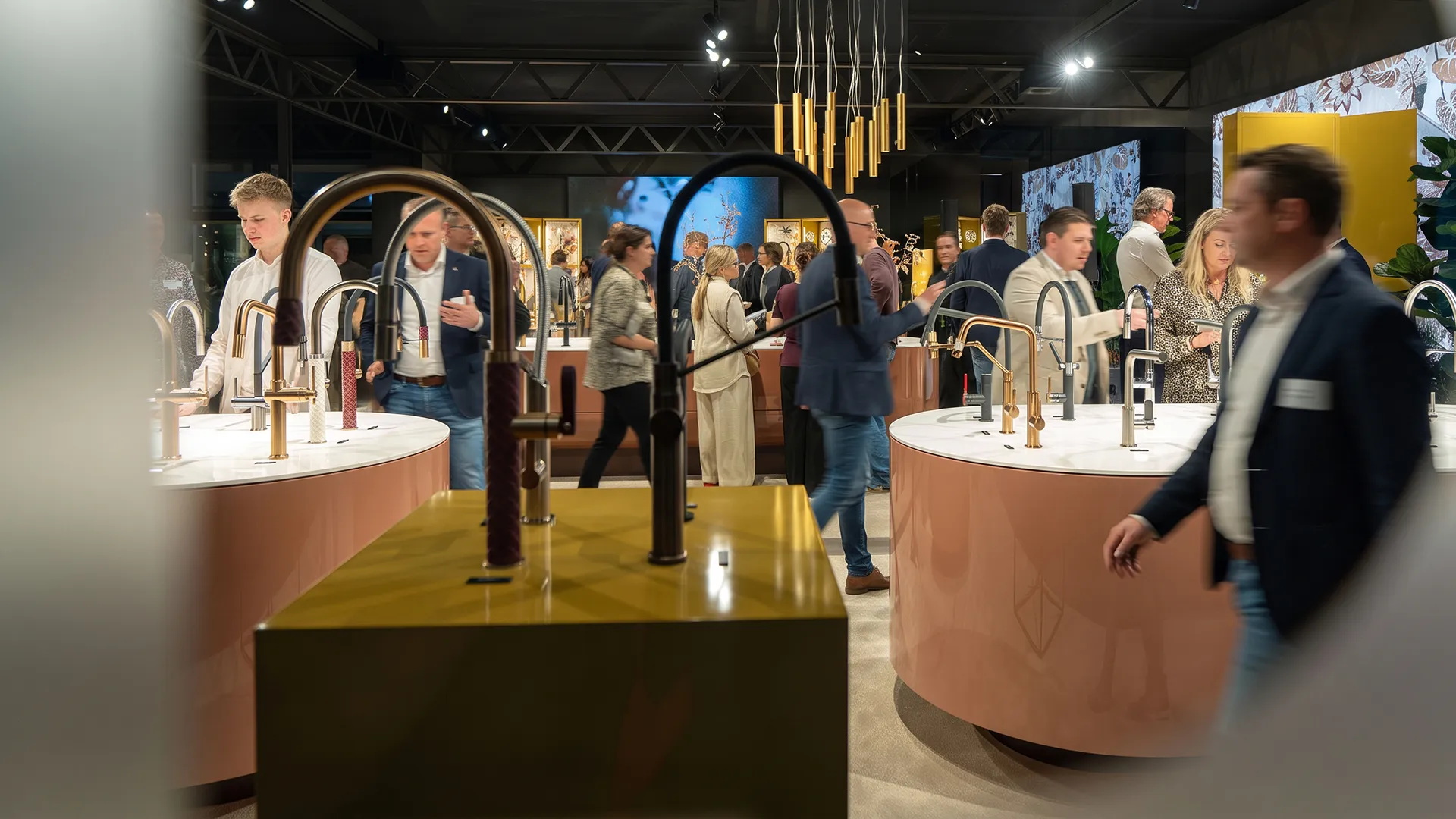 Visitors walking between tap displays on the Gessi stand, under gold pendant lights