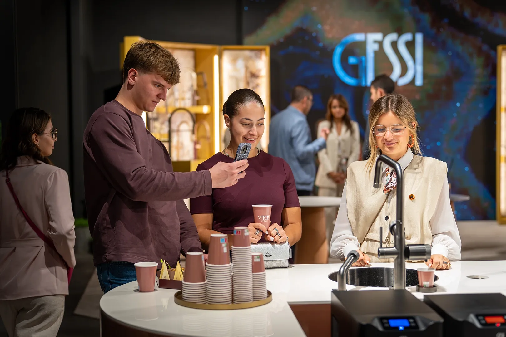 Visitors at a tap on the Gessi stand, with paper cups on the counter